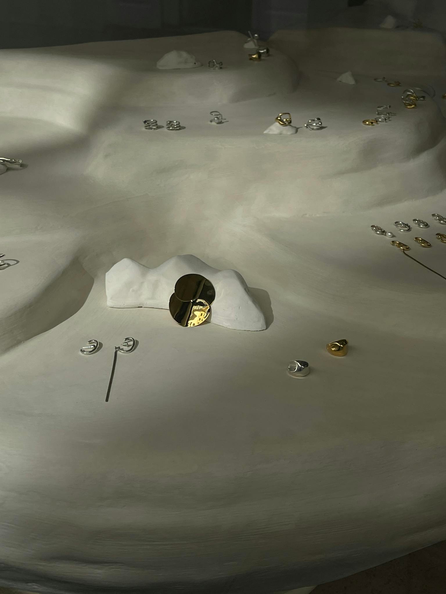 Artistic display of gold and silver jewelry on a textured abstract surface under soft lighting.